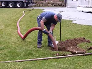 Septic pumping technician servicing a residential septic tank with a vacuum hose in Peoria, IL