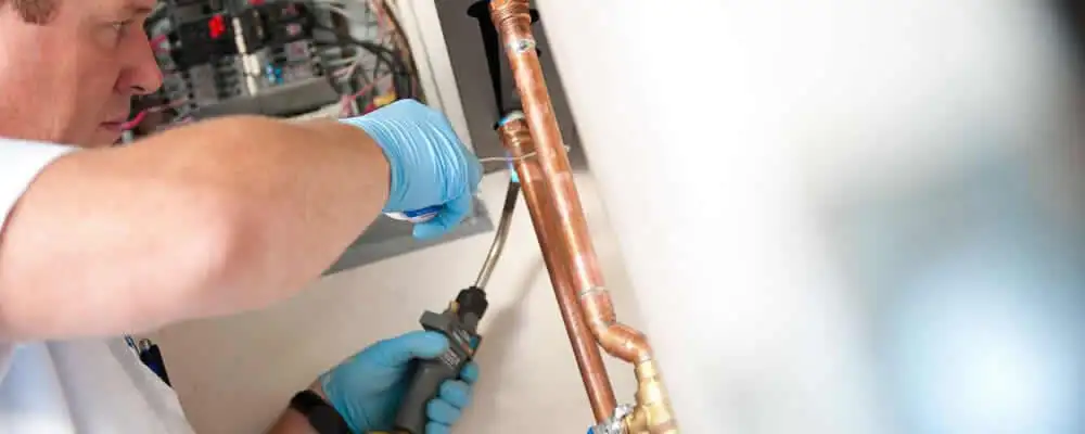 Water heater repair technician testing copper pipe connections and controls in Peoria, IL
